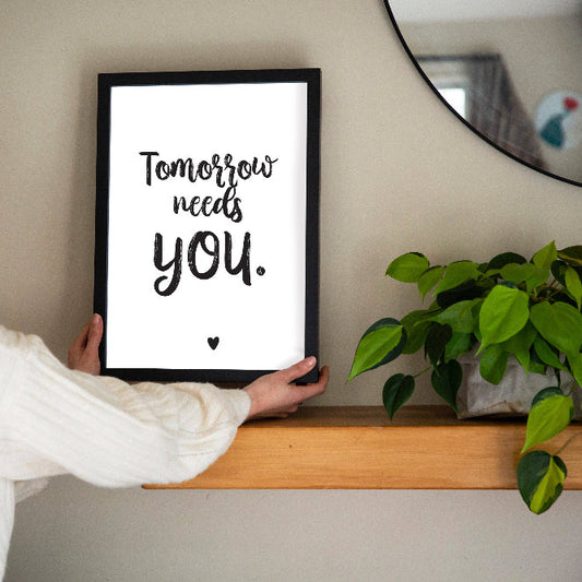 Person holding a framed quote Tomorrow needs you on a shelf with a plant in the background, designed by Paper Heart Design NZ to support suicide prevention and awareness