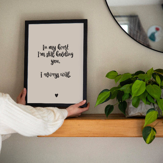 Brunette lady holding In My Heart memorial print in cream framed on wooden shelf with plant and mirror, grief and loss keepsake print by Paper Heart Design NZ
