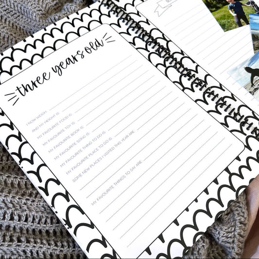 Little Me toddler milestone book open to three years old page with milestone prompts and photo space, flat lay on pink and grey fabric, by Paper Heart Design NZ