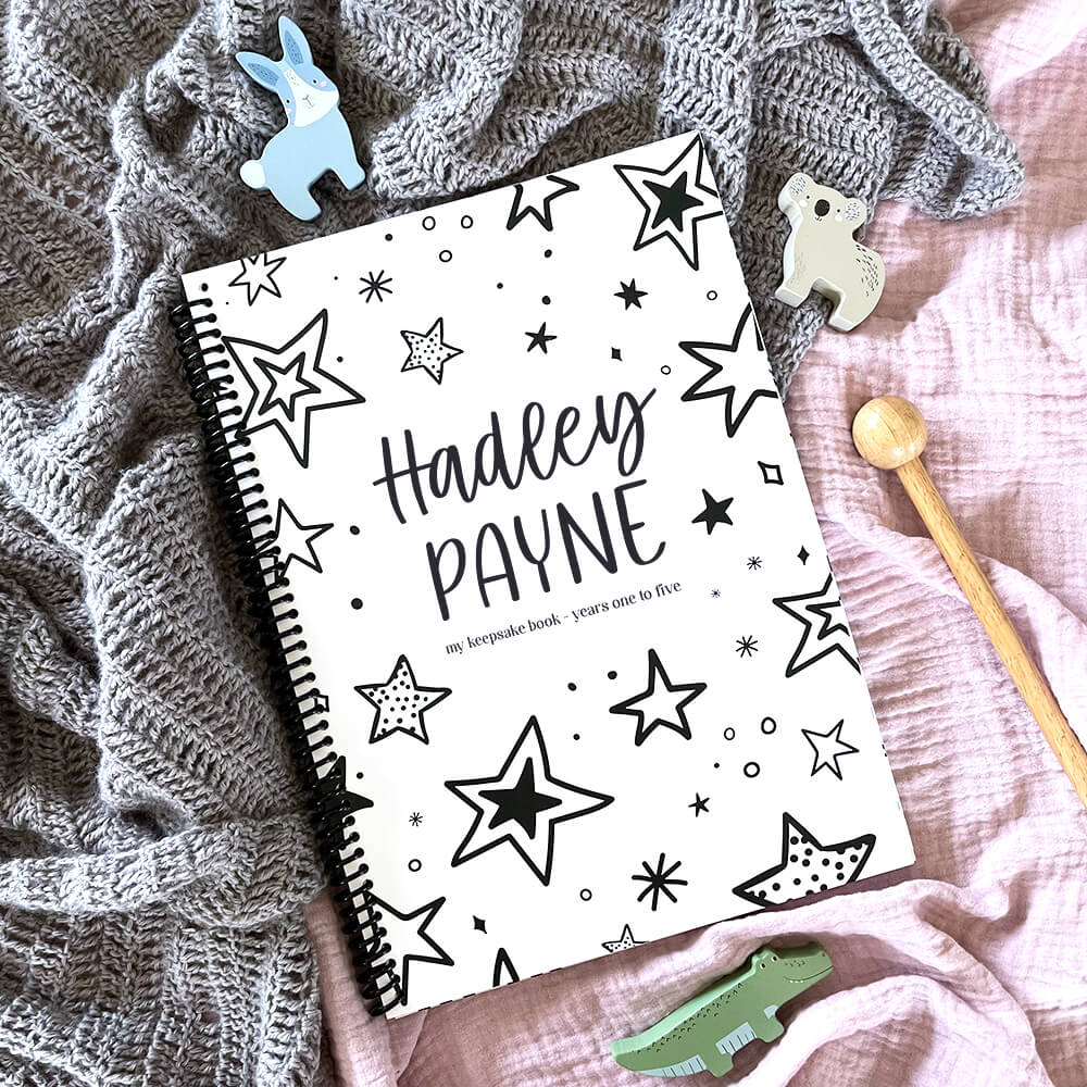 Personalised Little Me toddler milestone book with Stars design and child's name flat lay on pink and grey fabric with wooden toy animals, by Paper Heart Design NZ