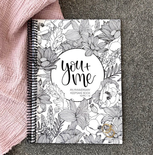 You and Me Anniversary keepsake book floral cover flat lay on pink and grey fabric with gold rings, anniversary gift by Paper Heart Design NZ