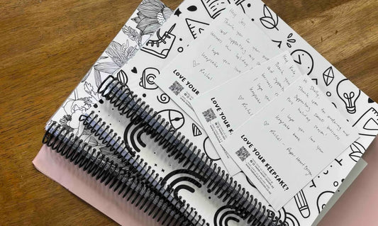 A stack of Paper Heart Design keepsake spiral bound notebooks on a wooden surface, with a pink postage bag under and three handwritten thank you note cards sitting on top, another year of keepsake books and personalised prints for New Zealand families