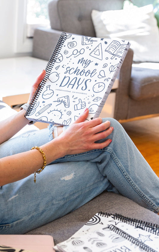 Person sitting in a living room holding My School Days Schoolies school record book with Paper Heart Design keepsake books beside them on the couch