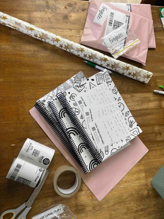 Paper Heart Design orders being packed in Wellington NZ with keepsake books, NZ Post courier labels and wrapping paper on wooden table