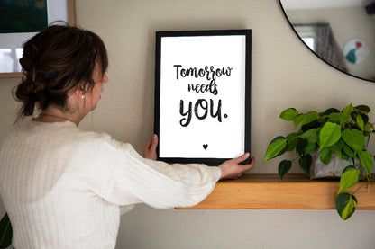 Person holding a framed quote Tomorrow needs you on a shelf with a plant in the background, designed by Paper Heart Design NZ to support suicide prevention and awareness