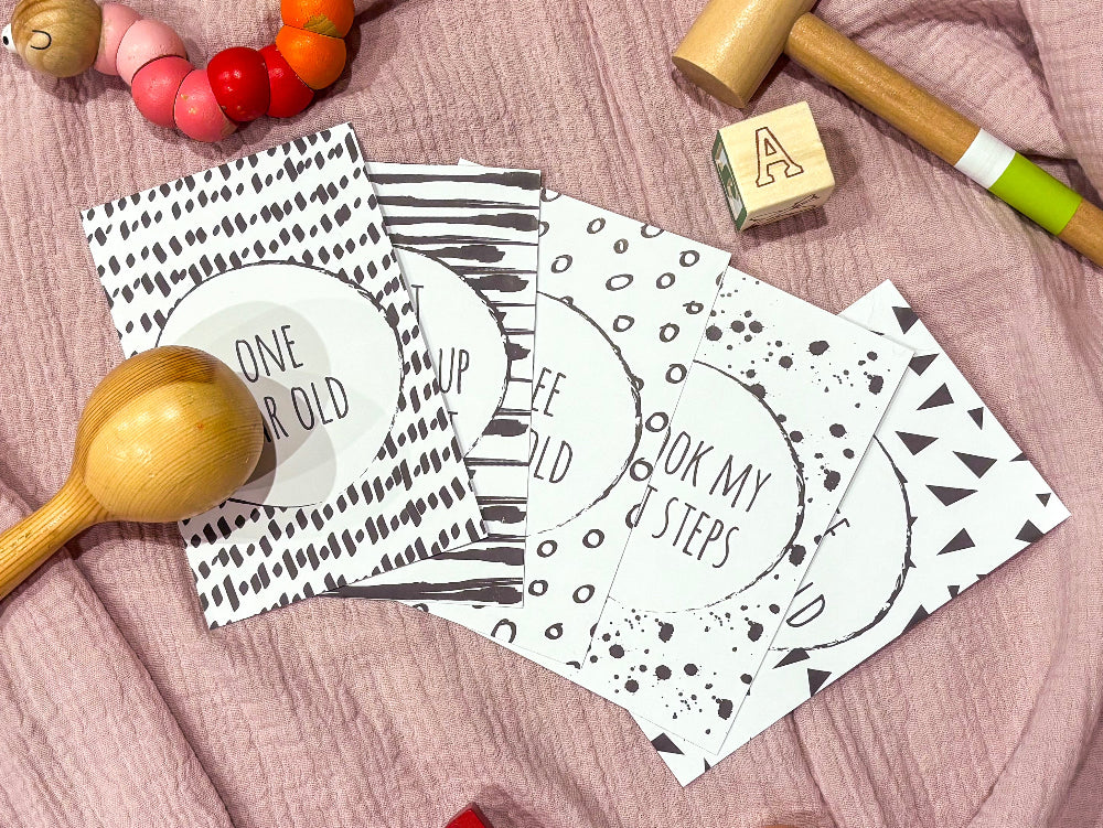 Downloadable baby milestone cards five black and white cards on pink fabric background with baby toys, printable first year keepsake by Paper Heart Design