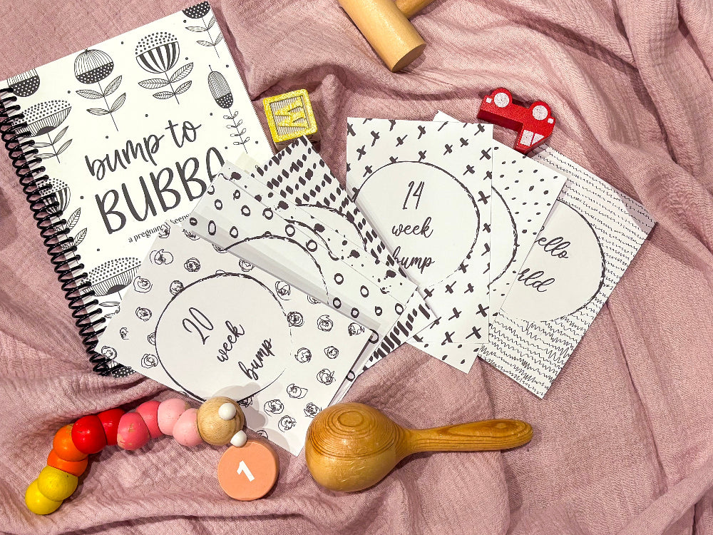 Downloadable bump milestone cards spread on Bump to Bubba pregnancy journal flat lay on pink fabric with baby toys, by Paper Heart Design