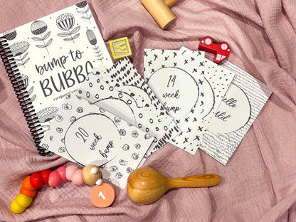 Downloadable bump milestone cards spread on Bump to Bubba pregnancy journal flat lay on pink fabric with baby toys, by Paper Heart Design