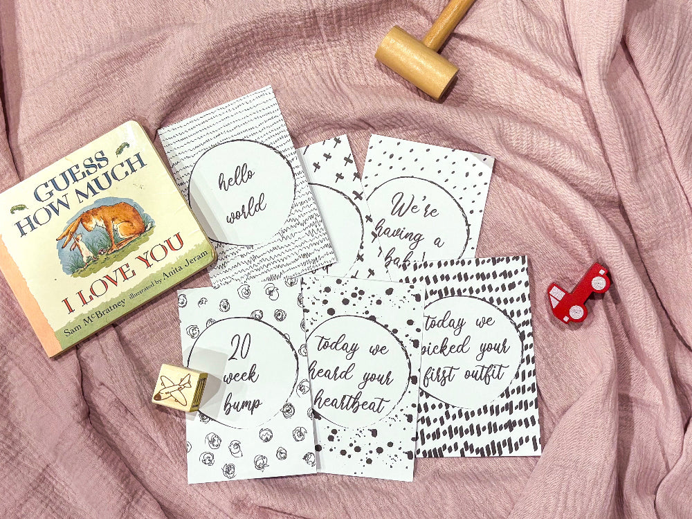 Downloadable bump milestone cards laid out on pink fabric with Guess How Much I Love You book and baby toys, printable pregnancy keepsake by Paper Heart Design