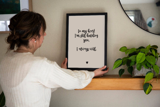 Brunette lady holding In My Heart memorial print in cream framed on wooden shelf with plant and mirror, grief and loss keepsake print by Paper Heart Design NZ