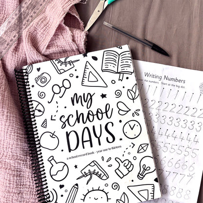 My School Days school record book Schoolies cover flat lay on pink fabric with scissors, pen , ruler and Writing Numbers worksheet visible beside it, by Paper Heart Design NZ