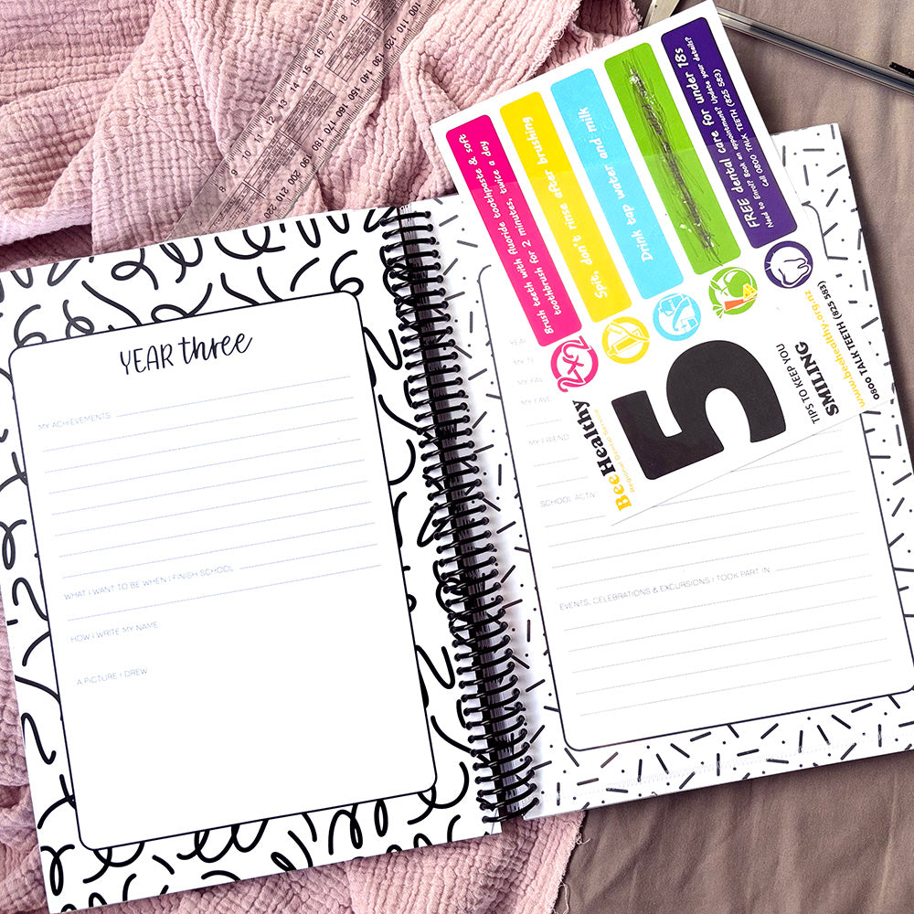 My School Days school record book open to Year Three spread showing lined journalling and prompt page and premium clear pocket with certificate, flat lay on pink fabric with pen and ruler in background, by Paper Heart Design NZ