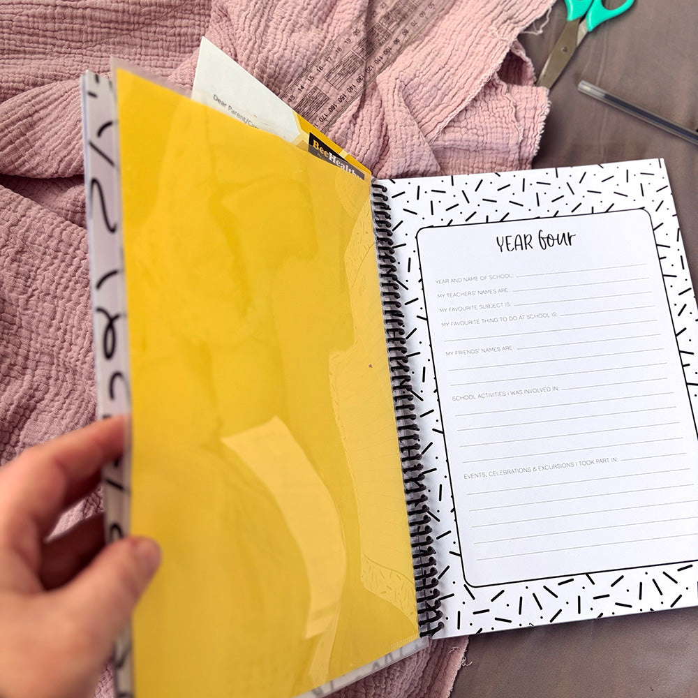 My School Days school record book open to Year Four double page spread with yellow plastic pocket held open showing school notes stored inside, spiral binding and decorated lined page visible, by Paper Heart Design NZ