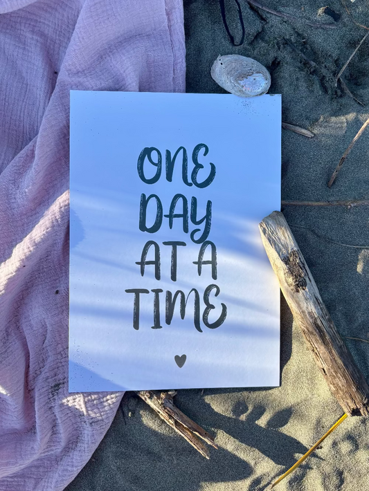 One Day at a Time typographic print in sage on pink towel and sand, beach lifestyle flat lay by Paper Heart Design NZ