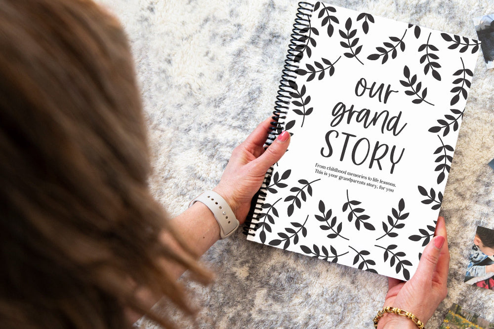 Our Grand Story grandparent keepsake book held by brunette woman over grey rug, grandparent memory book by Paper Heart Design NZ