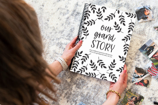 Our Grand Story grandparent keepsake book held by brunette woman over grey rug with baby and family photos around, grandparent memory book by Paper Heart Design NZ
