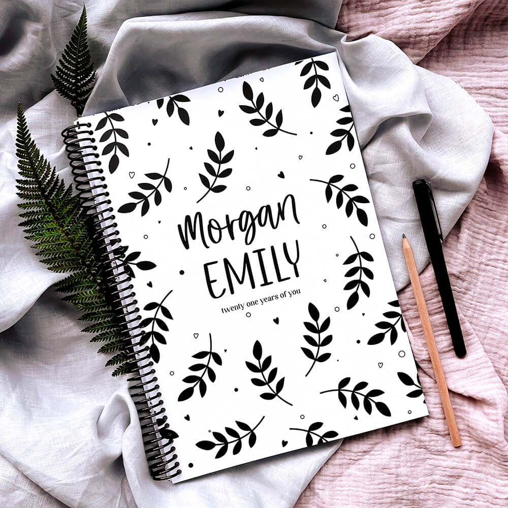 Personalised 21 Years Keepsake Book ferns cover flat lay on pink and grey fabric, with fern leaves, pencil and pen around, a custom birthday letter keepsake by Paper Heart Design NZ
