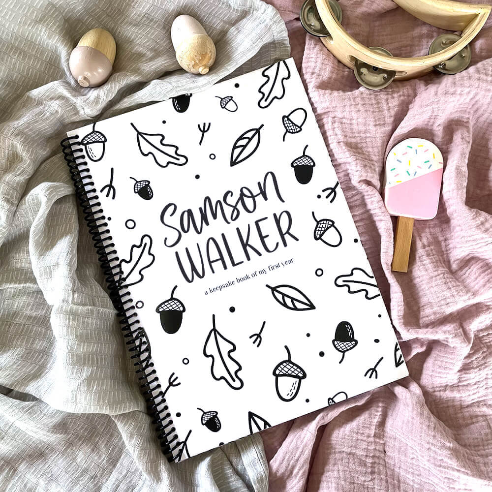 Personalised Hey Baby milestone book with acorns cover showing child's name on pink and grey textured fabric, custom baby keepsake by Paper Heart Design NZ