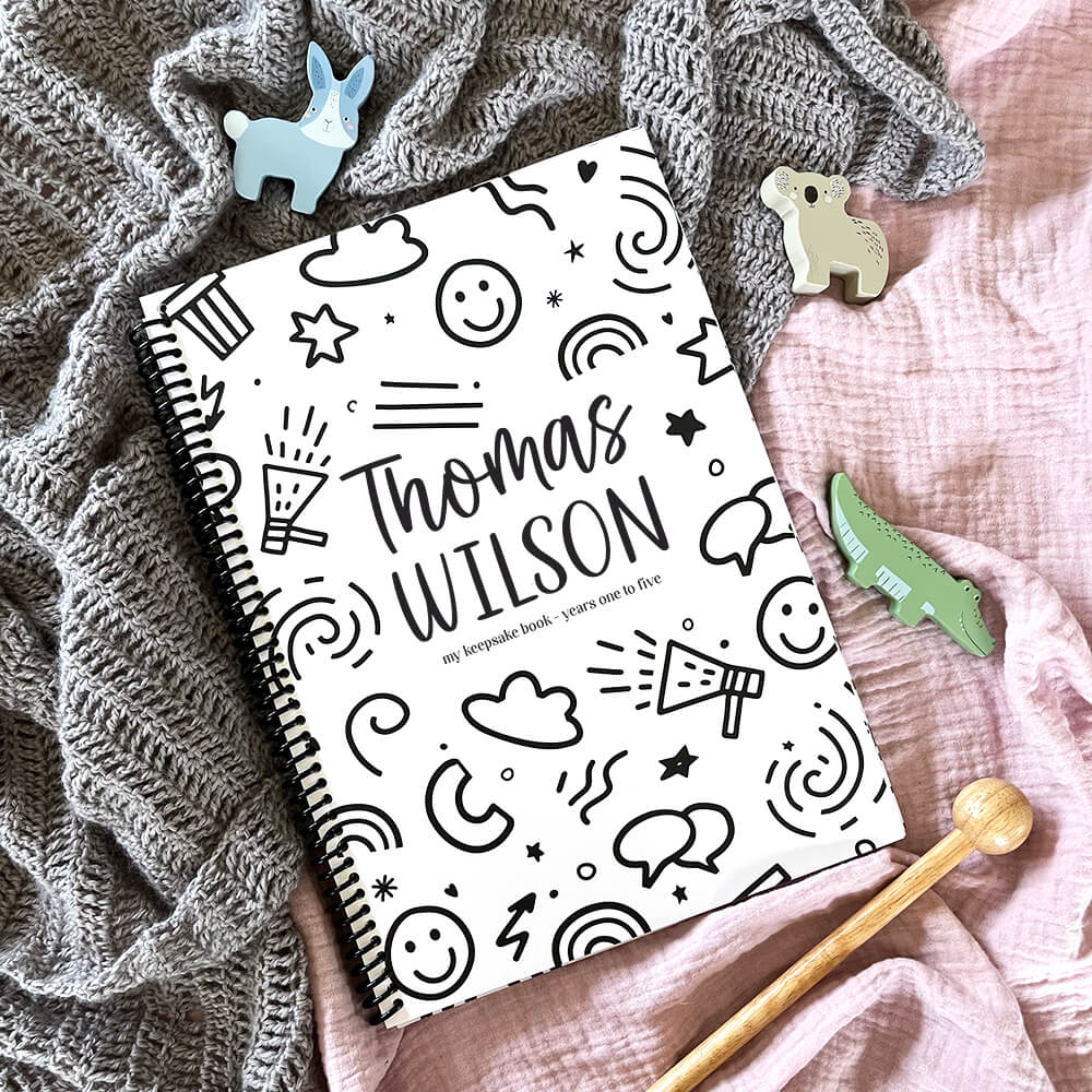 Personalised Little Me toddler milestone book with Smiles design and child's name flat lay on pink and grey fabric with wooden toy animals, by Paper Heart Design NZ