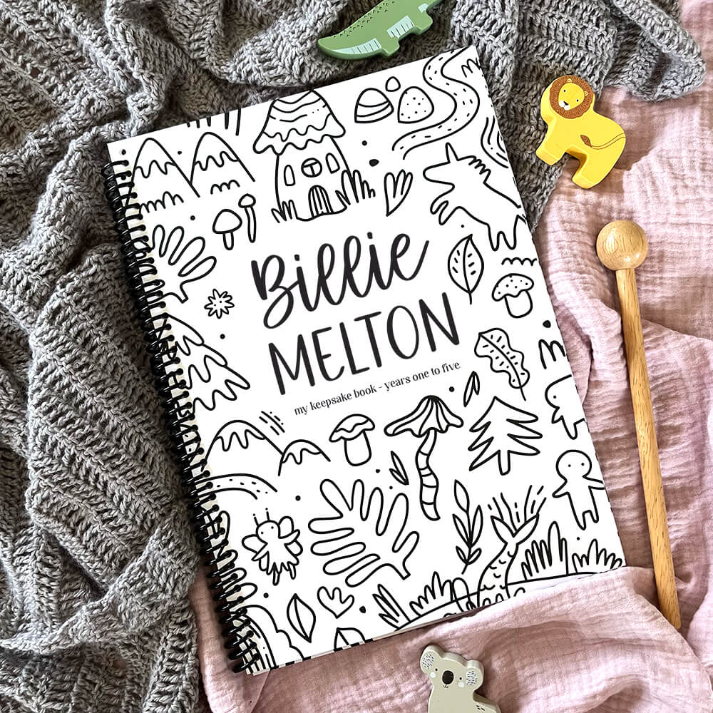 Personalised Little Me toddler milestone book with Wonderland design and child's name flat lay on pink and grey fabric with wooden toy animals, by Paper Heart Design NZ