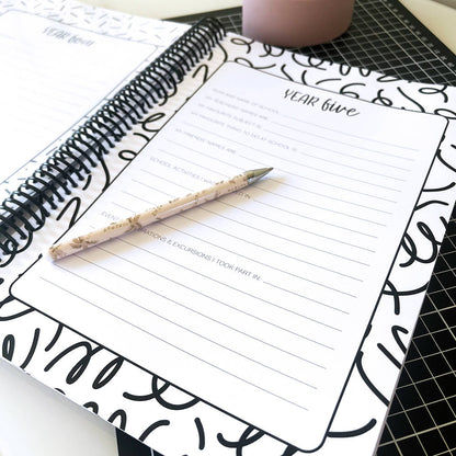Personalised My School Days school record book close up of unfilled year five page with pen on top, sitting on black grid mat and white surface, by Paper Heart Design NZ