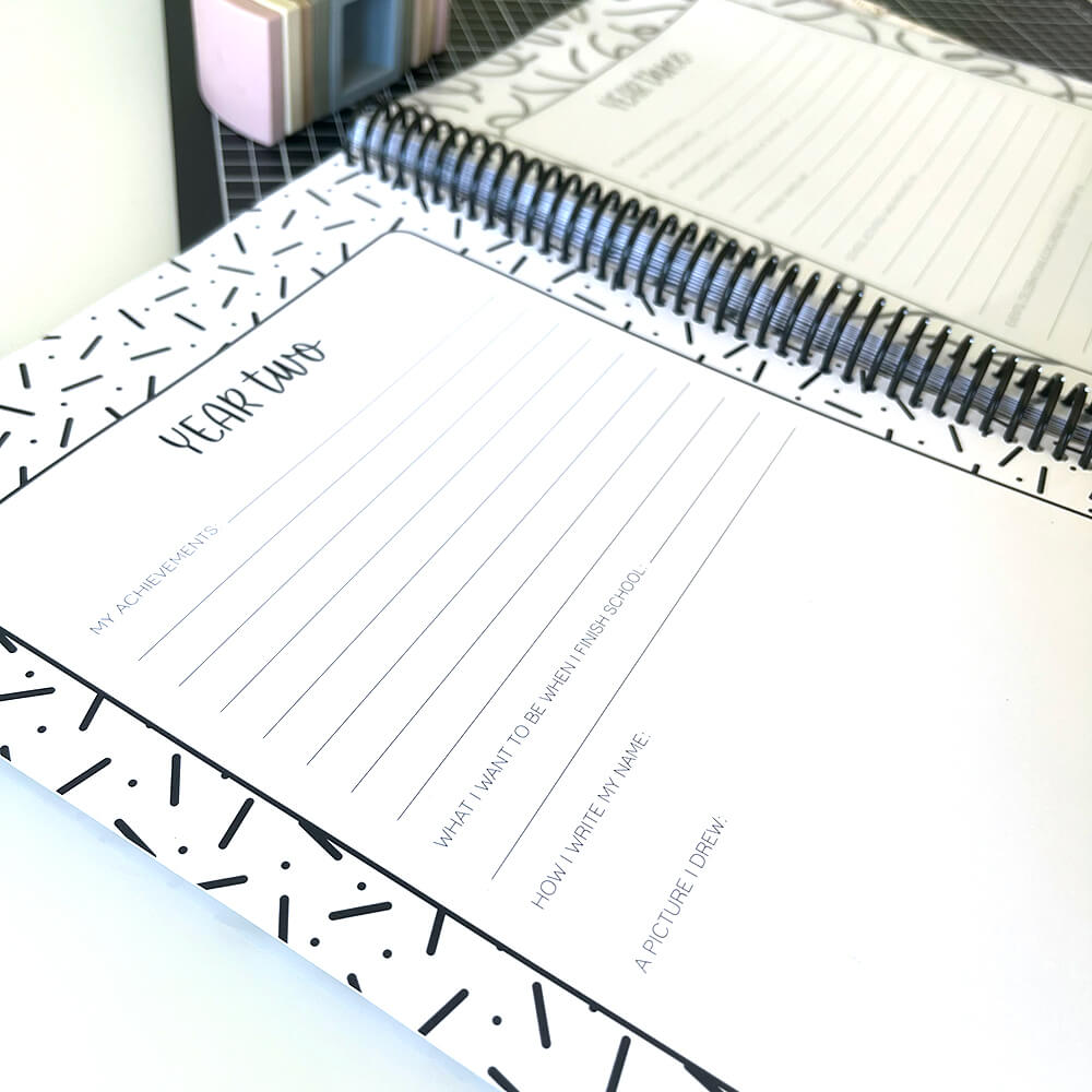 Personalised My School Days school record book close up of blank year two page with year three page behind, sitting on black grid mat and white surface, by Paper Heart Design NZ