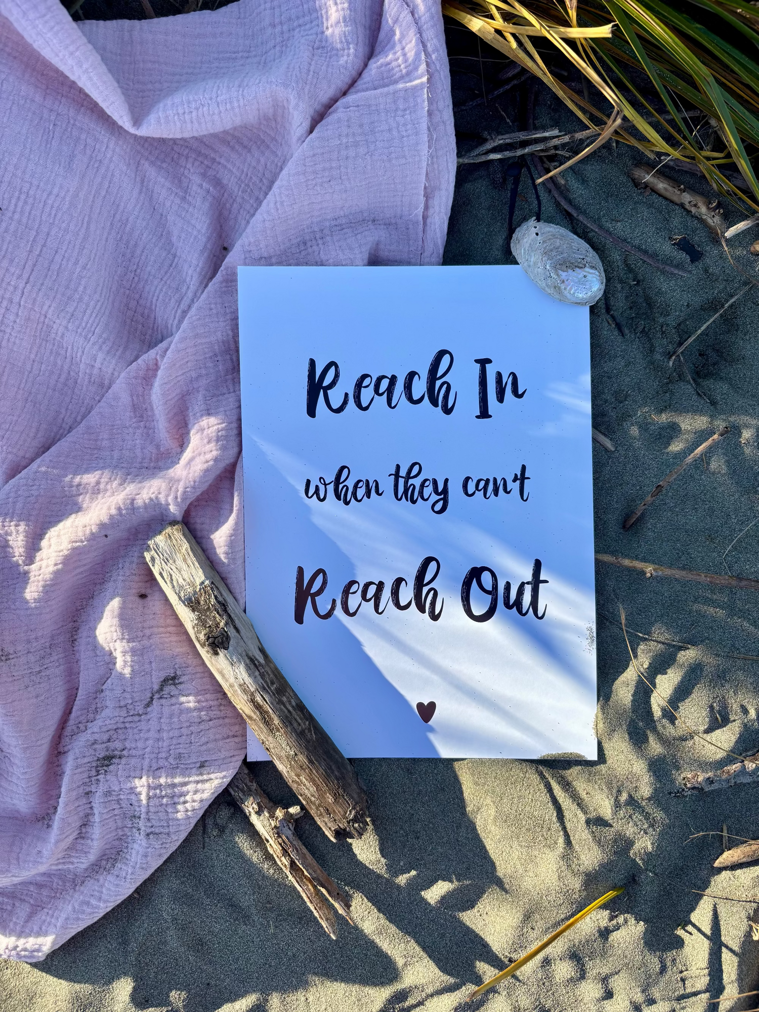 Reach In When They Can't Reach Out print in black on white page flat lay on sand and pink towel with driftwood and shell, Hope Collection by Paper Heart Design NZ