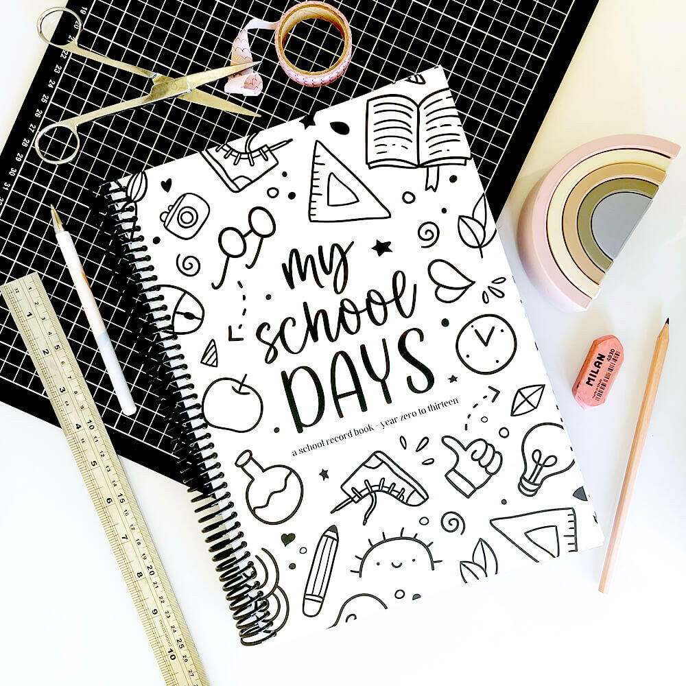 School Record Book with Schoolies cover flat lay on black grid mat and white surface surrounded by washi tape, pen, scissors, ruler, pencil and eraser, by Paper Heart Design NZ