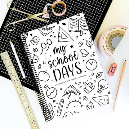 School Record Book with Schoolies cover flat lay on black grid mat and white surface surrounded by washi tape, pen, scissors, ruler, pencil and eraser, by Paper Heart Design NZ