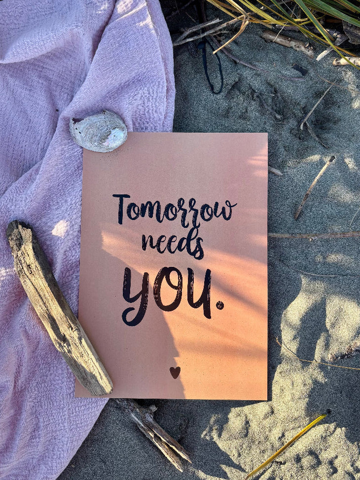 Tomorrow Needs You print in black on clay flat lay on sand and pink towel with seaweed, driftwood and shells, Hope Collection supporting mental health and suicide prevention by Paper Heart Design NZ