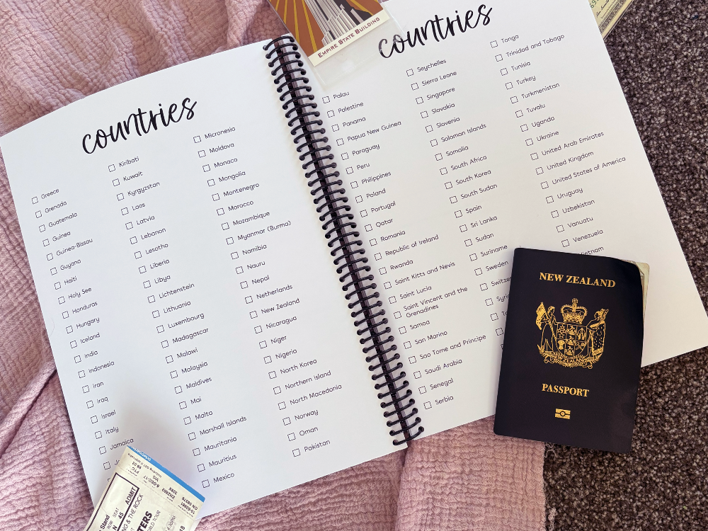 Travel Adventures keepsake journal open to countries checklist page flat lay on pink and grey surface with passport and tickets, by Paper Heart Design NZ
