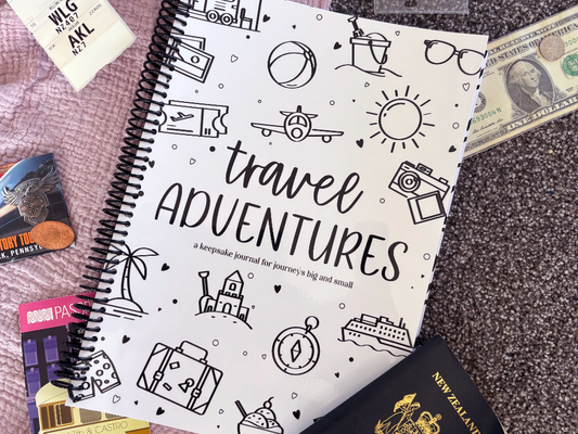 Travel Adventures keepsake journal front cover flat lay on pink and grey fabric with passport, tickets and US money, travel keepsake by Paper Heart Design NZ