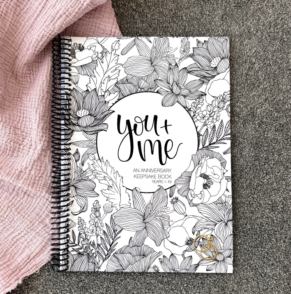 You and Me Anniversary keepsake book floral cover flat lay on pink and grey fabric with gold rings, anniversary gift by Paper Heart Design NZ