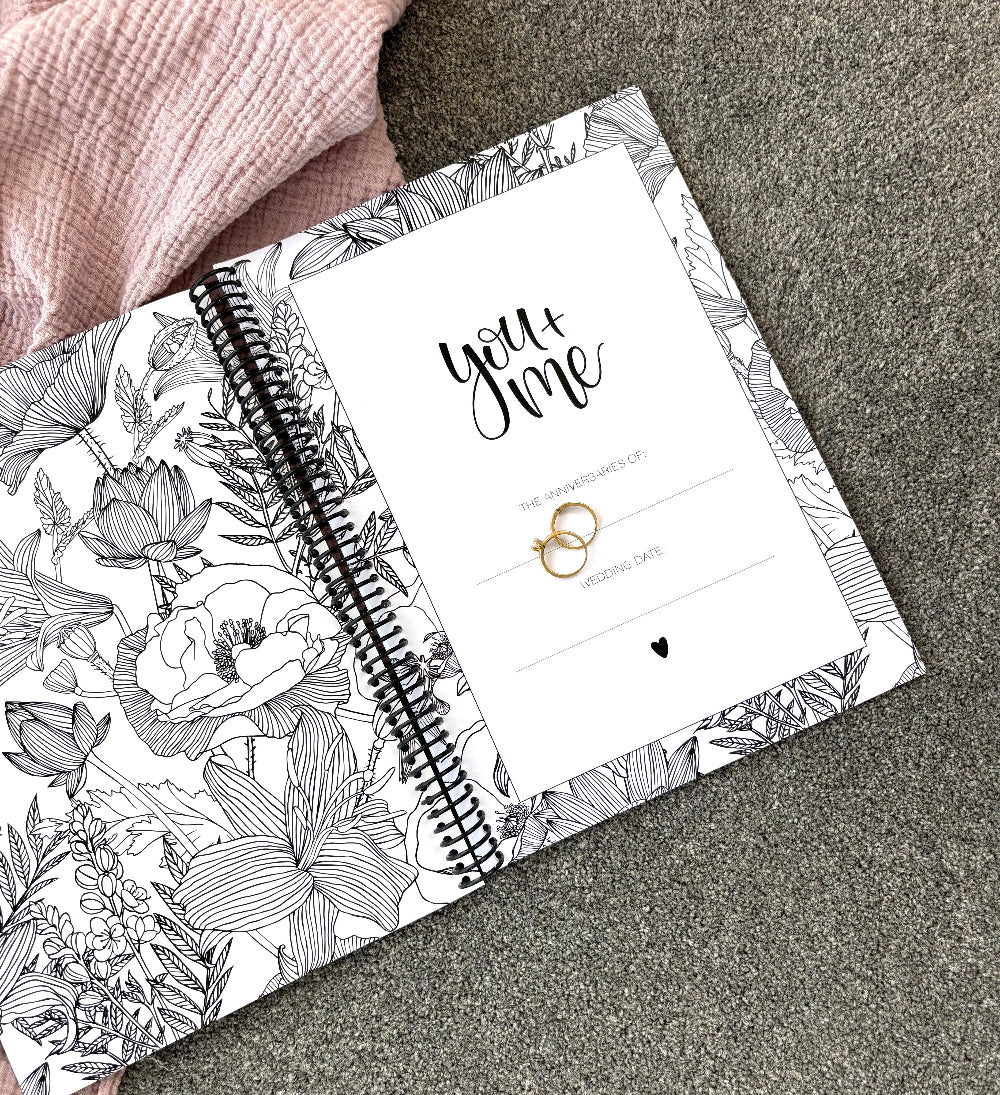 You and Me Anniversary keepsake book open to first page showing book title and floral inner cover with gold ring set on pink and grey fabric, by Paper Heart Design NZ