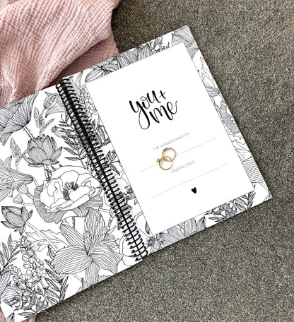 You and Me Anniversary keepsake book open to first page showing book title and floral inner cover with gold ring set on pink and grey fabric, by Paper Heart Design NZ