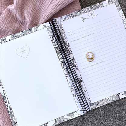 You and Me Anniversary keepsake book open to year three page spread with milestone prompts and photo space, gold rings on pink and grey fabric, by Paper Heart Design NZ