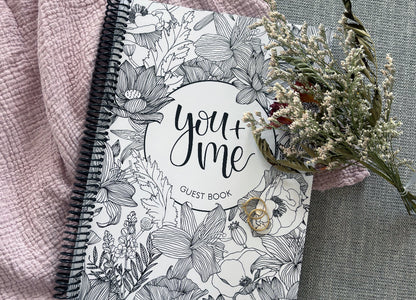 You and Me wedding guest book floral cover surrounded by dried flowers on textured surface, wedding keepsake by Paper Heart Design NZ