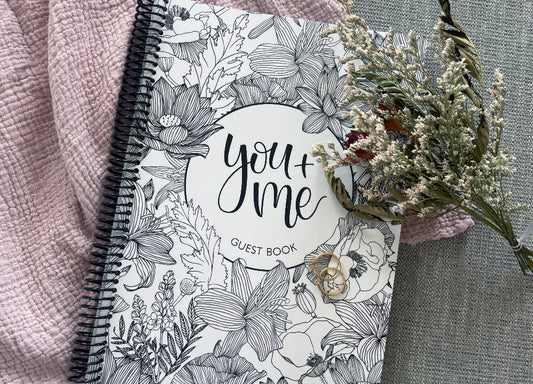 You and Me wedding guest book floral cover surrounded by dried flowers on textured surface, wedding keepsake by Paper Heart Design NZ