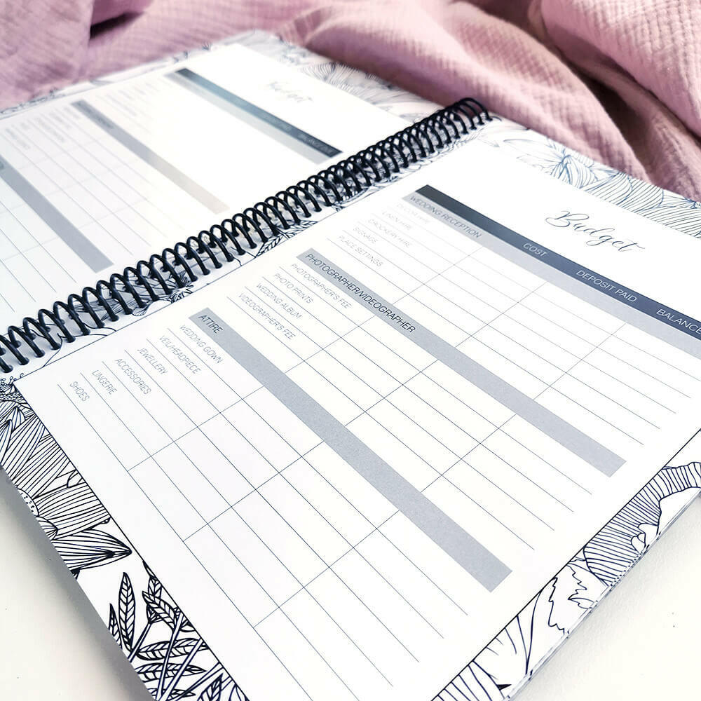 You and Me wedding planner open to budget checklist pages on pink textured background, NZ wedding planning book by Paper Heart Design