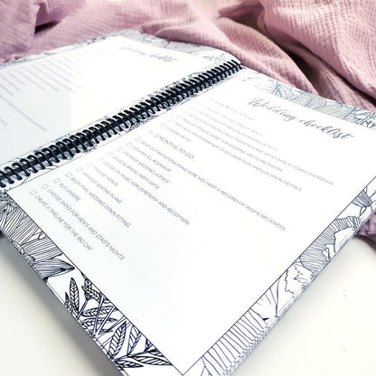 You and Me wedding planner open to wedding checklist pages on pink textured background, NZ wedding planning book by Paper Heart Design